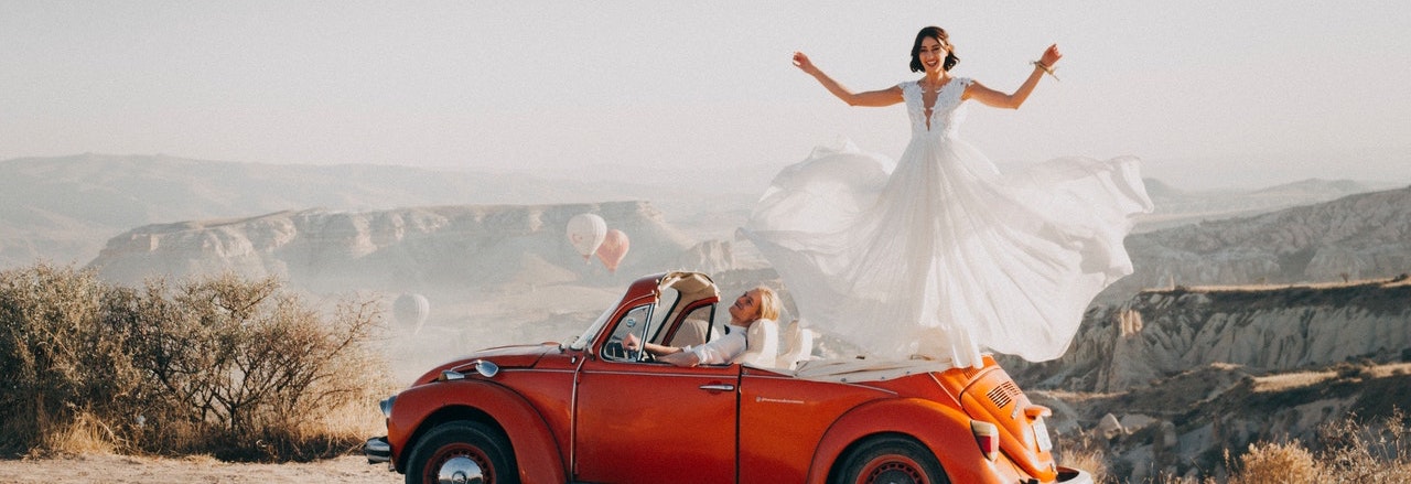 Dame habillée en robe de marieé debout sur une voiture